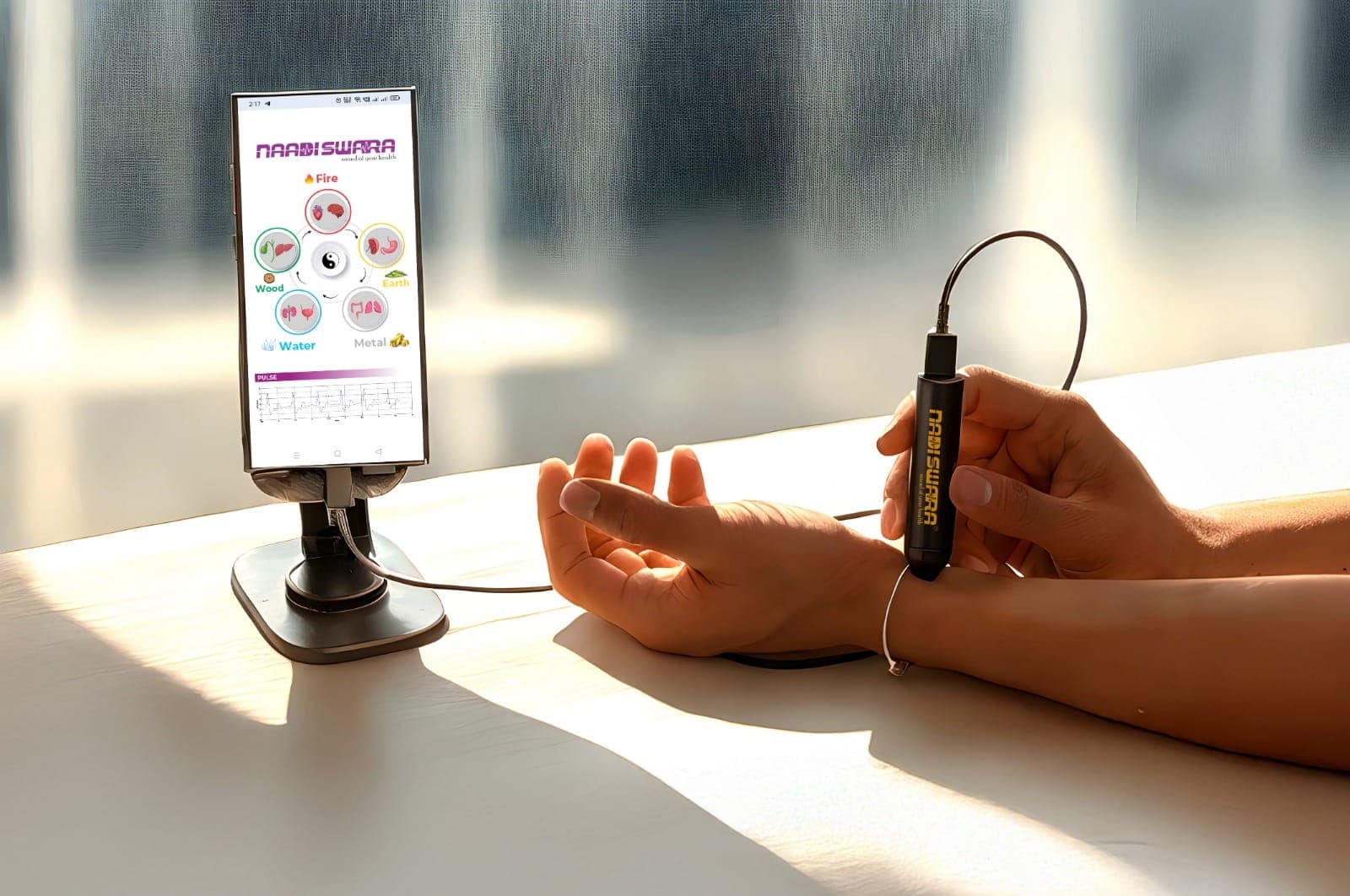 The Nadiswara pulse sensor held on a wrist, next to a phone showing the Nadiswara app